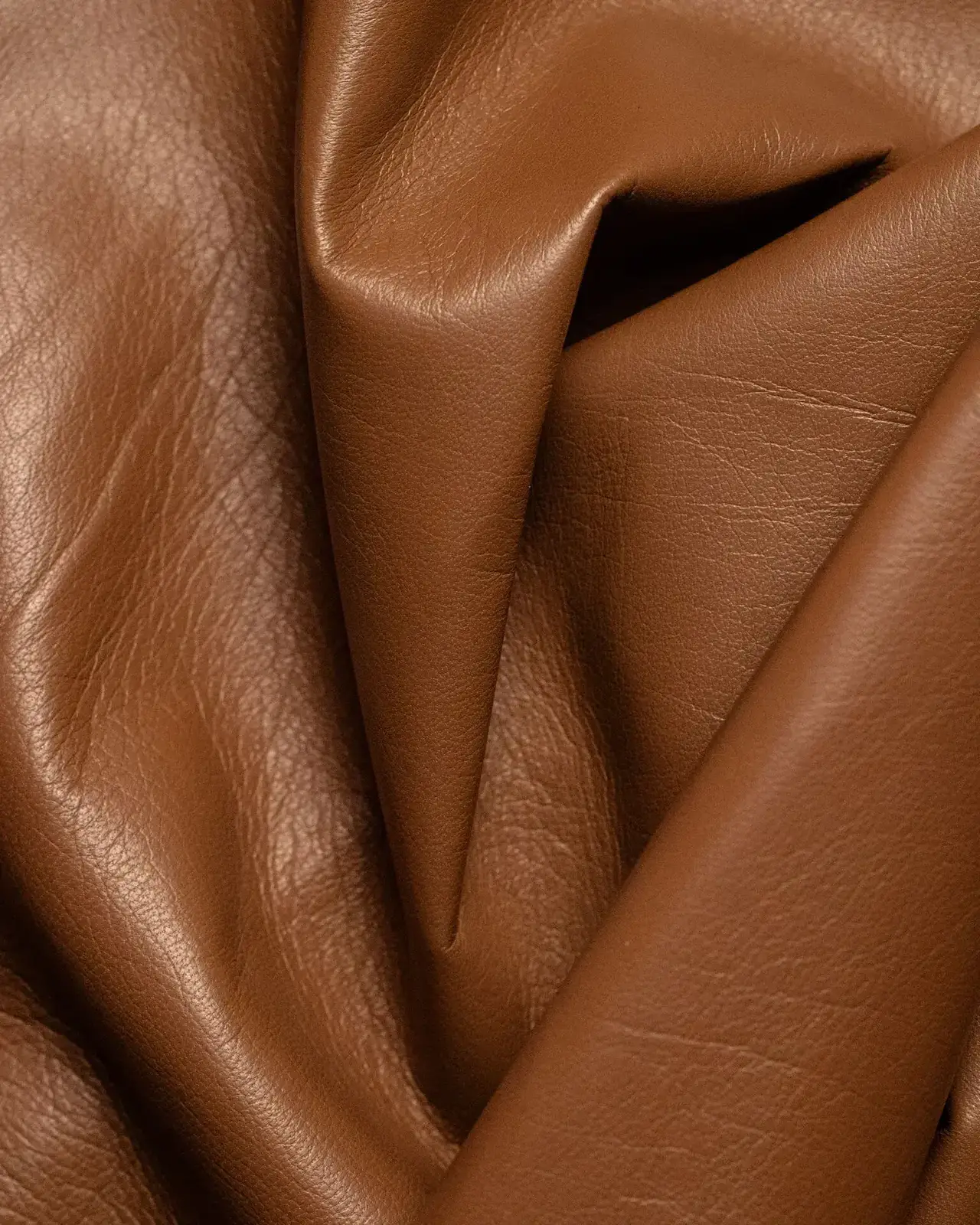 Macro of a brown leather hide folded into soft creases, fine natural grain lines visible across the surface